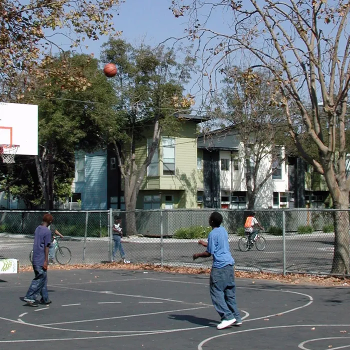 Kids playing basketball at the basketball court with Magnolia Row in West Oakland, California in the background.